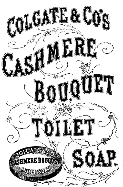 Line engraving in black and white. The words “Colgate & Co's Cashmere Bouquet Toilet Soap” are set in heavy shaded capitals arranged in five curving bands across the sheet, with fine engraved scrollwork and small flower sprays drawn behind the lettering. At the lower left an oval cake of soap is shown in perspective, its top stamped with the same brand wording.