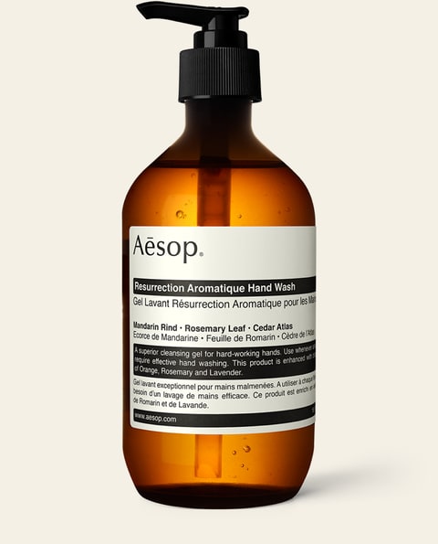 Photograph of a 500 millilitre amber glass pump bottle of Aesop Resurrection Aromatique Hand Wash on a plain white background. A rectangular label carries the product name and ingredient text in small type arranged in tight horizontal bands.